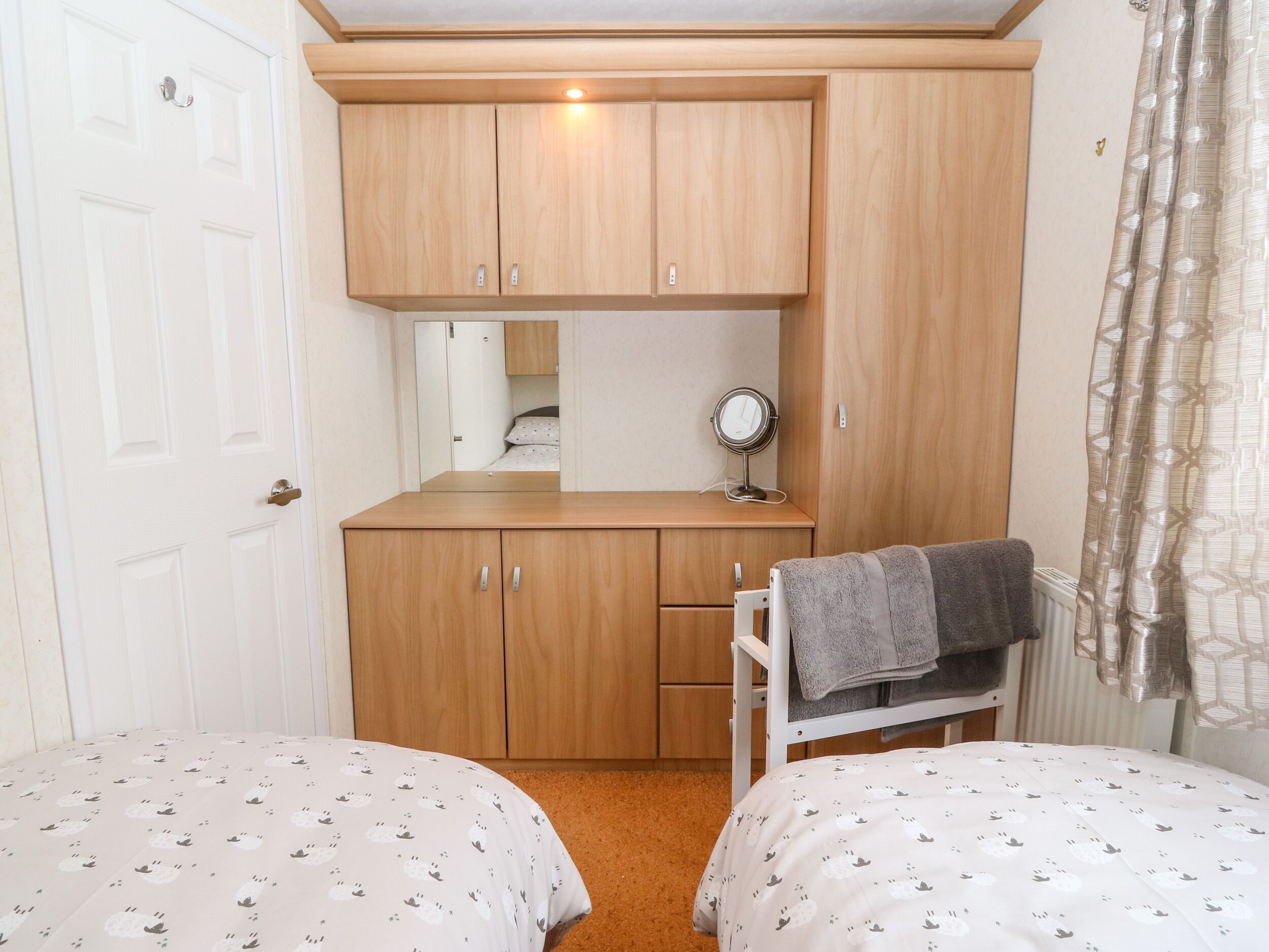 A bedroom with two beds, a wooden wardrobe, a mirror, and a radiator.