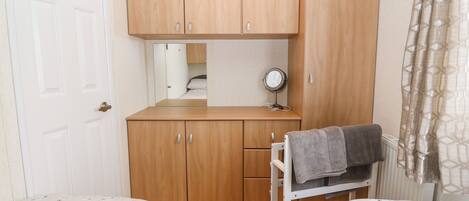 A bedroom with two beds, a wooden wardrobe, a mirror, and a radiator.