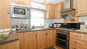 A modern kitchen with wooden cabinets, a stainless steel microwave, a gas stove, and various kitchen utensils. - Gwel Y Môr (Caernarfon)