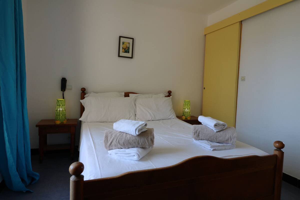 Un lit bien fait, avec des serviettes, une table de chevet avec une lampe et un tableau au mur.