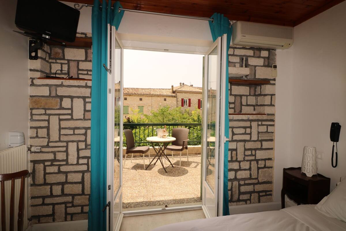 Une chambre comprenant un lit, une petite table avec des chaises, un téléphone et donnant sur un balcon équipé d’une table et de chaises.