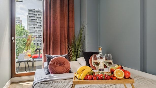 A modern living room with a sofa, a wooden coffee table with fruits and drinks, and a balcony with a laptop and a chair. - Lumina apartment with balcony Warsaw (Warsaw)