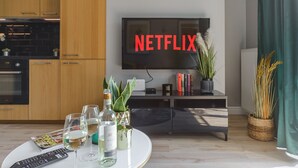 A modern living room with a flat-screen TV displaying "NETFLIX," a round coffee table with a remote control, wine glasses, and decorative items. - Lumina apartment with balcony Warsaw (Warsaw)