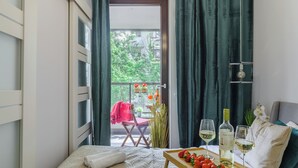 A bedroom with a bed, a table with strawberries and wine glasses, and a view of a balcony with plants and a chair. - Lumina apartment with balcony Warsaw (Warsaw)
