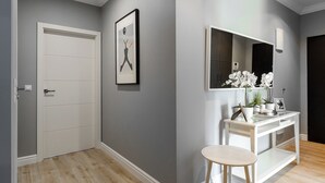 A hallway with a white door, a framed artwork, a vanity with a mirror, a small stool, and a potted plant. - Lumina apartment with balcony Warsaw (Warsaw)