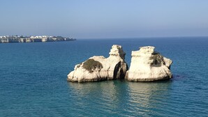 Vista despejada de una zona costera con formaciones rocosas blancas en el mar, una costa lejana con edificios y aguas tranquilas.