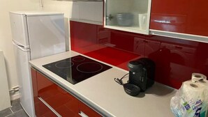 A compact kitchen with a white refrigerator, a red backsplash, a black electric stove, and a coffee maker on the counter. - Appartement T4 Rouen (Rouen)