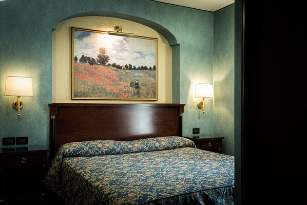 Habitación de hotel con una cama grande, dos lámparas de noche, un cuadro sobre la cama y un cabecero de madera.