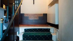 Una escalera con alfombra verde estampada, un símbolo fijado en la pared y cuadros enmarcados.