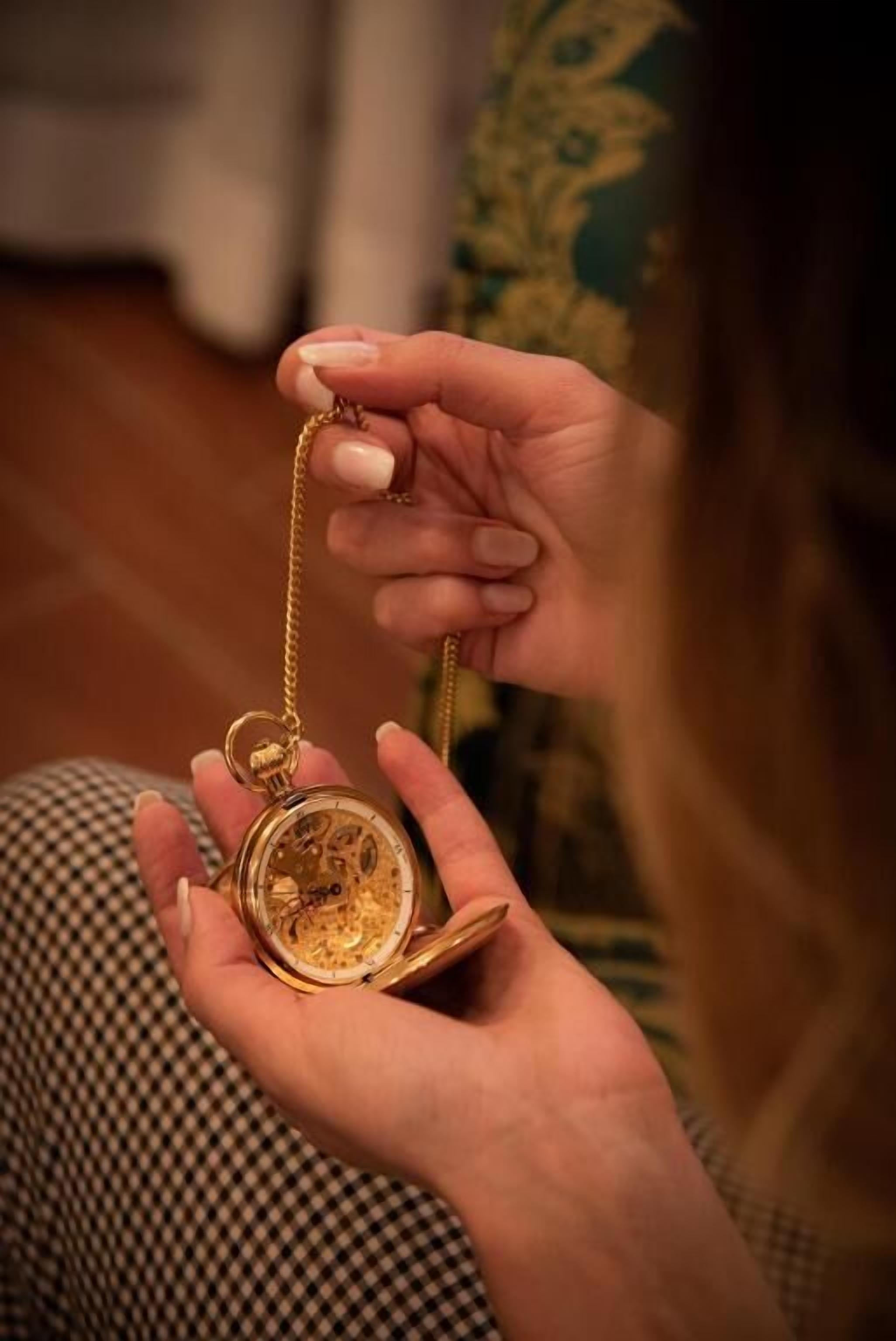 A person holding a gold pocket watch with a chain.