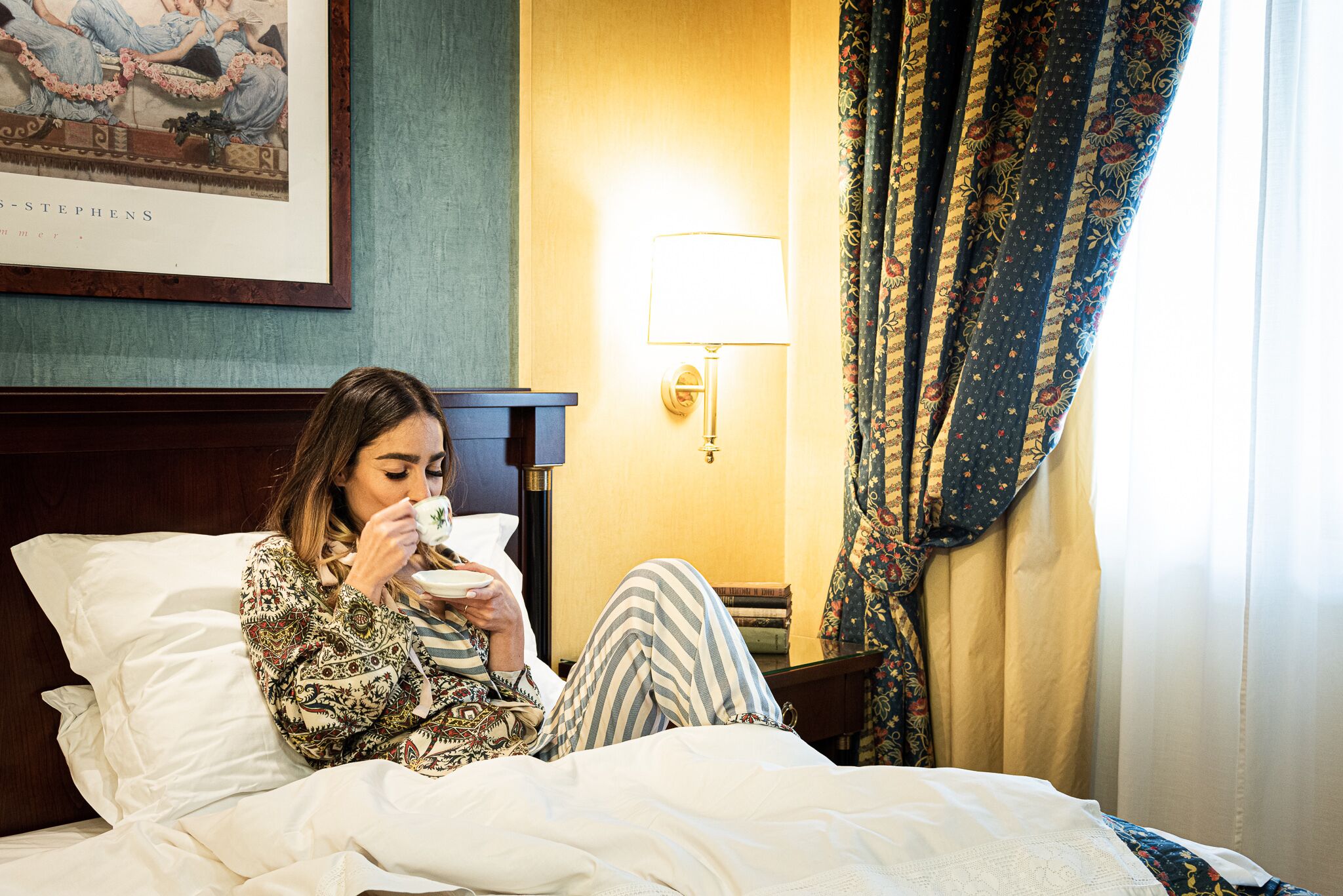 Iemand zit op een bed in een hotelkamer en houdt een kop vast.