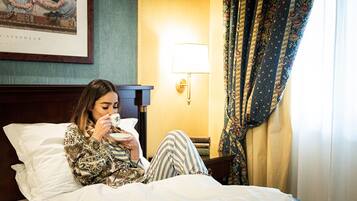 Iemand zit op een bed in een hotelkamer en houdt een kop vast.