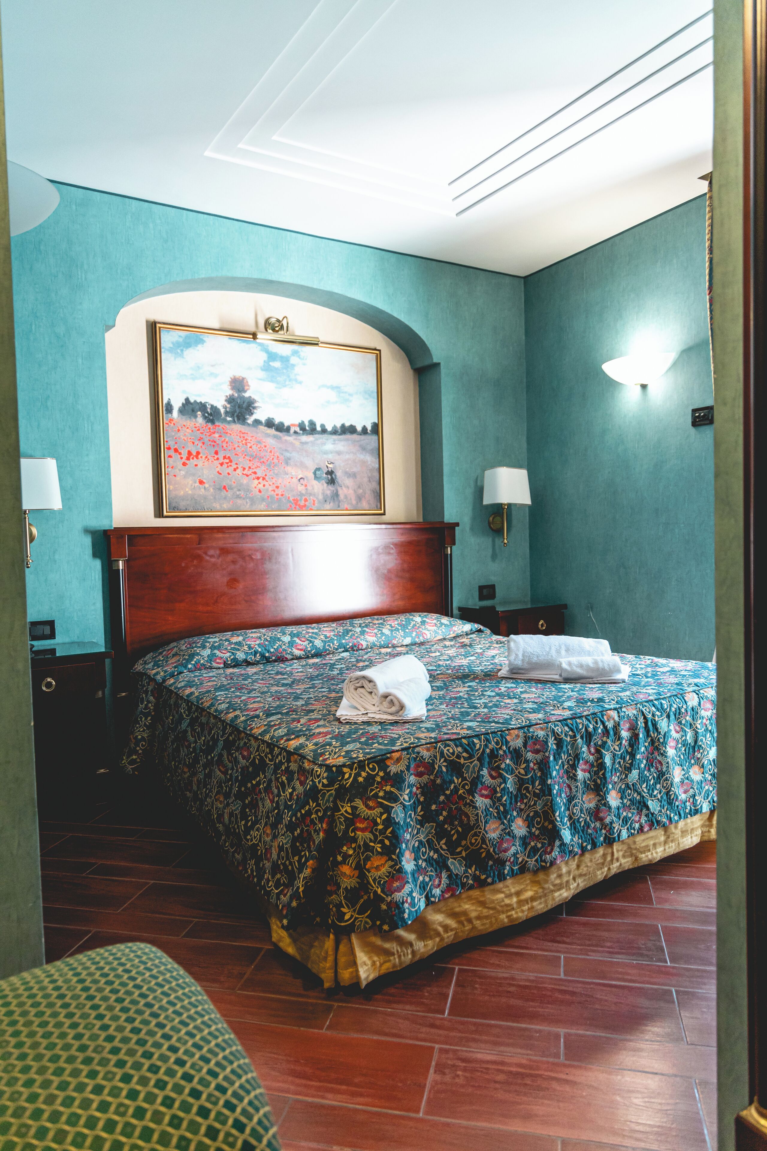 A hotel room with a large bed, a painting above the bed, and two bedside lamps.