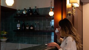 Una persona de pie frente a la barra de un bar, en una habitación con un salpicadero de azulejos y estantes con botellas.