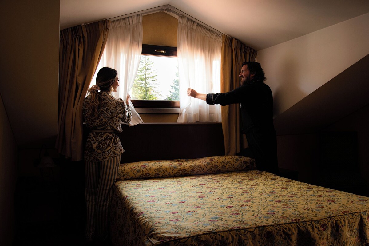 A bedroom with a bed, a window with curtains, and a view of trees outside.