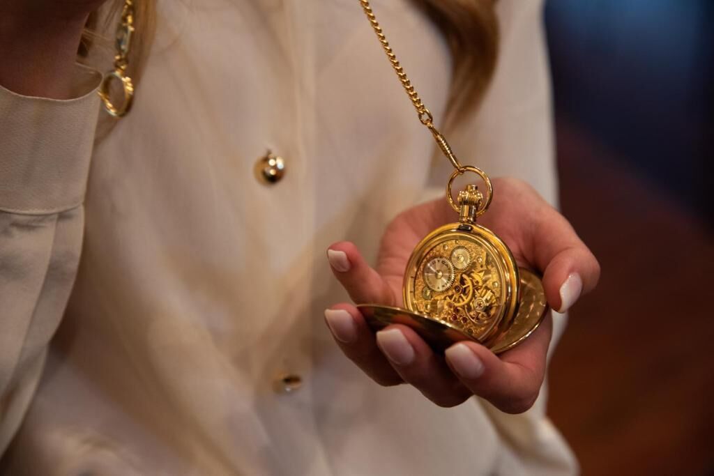 A person holding a gold pocket watch with a chain.