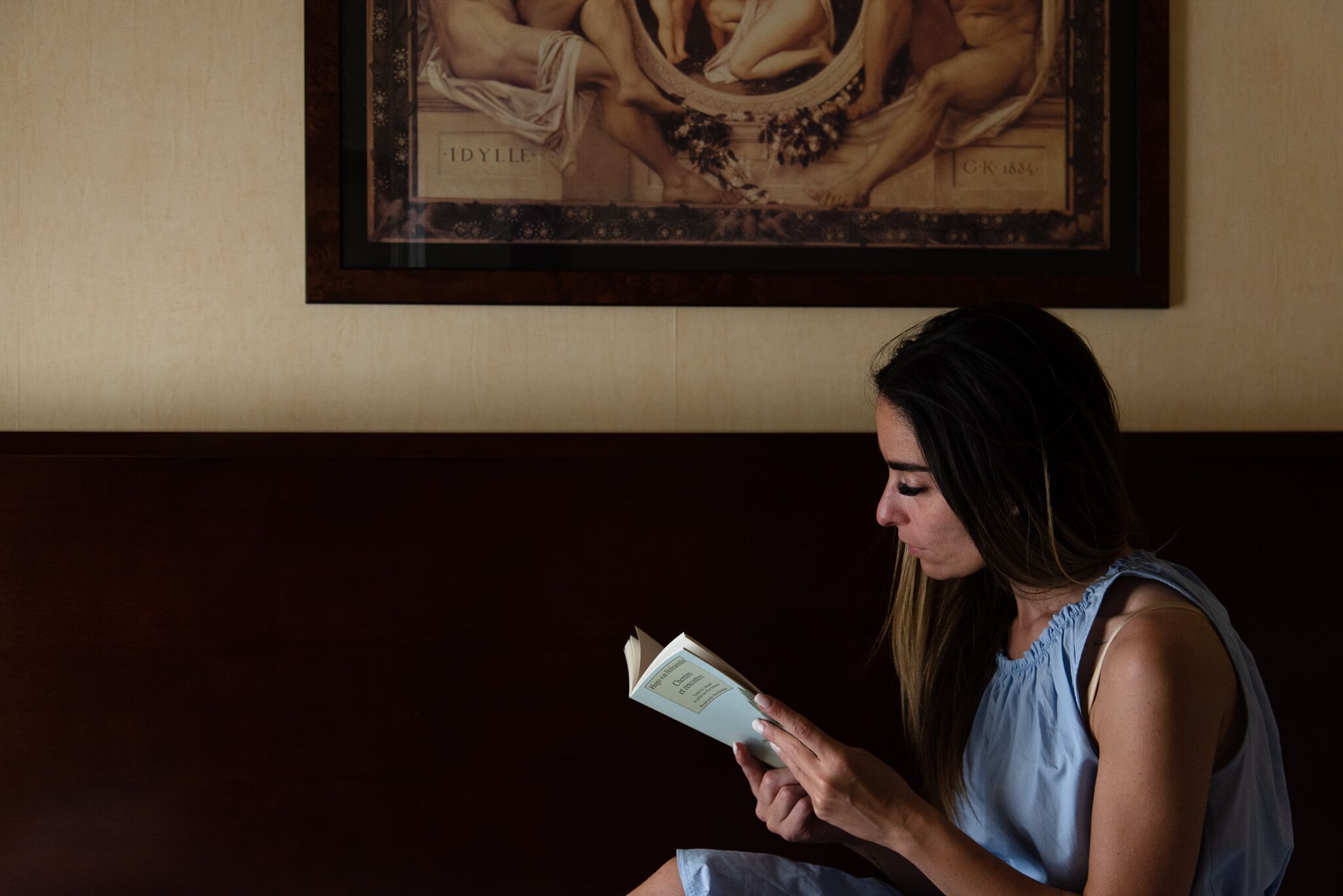 A person sitting on a dark-colored bench, reading a book.
