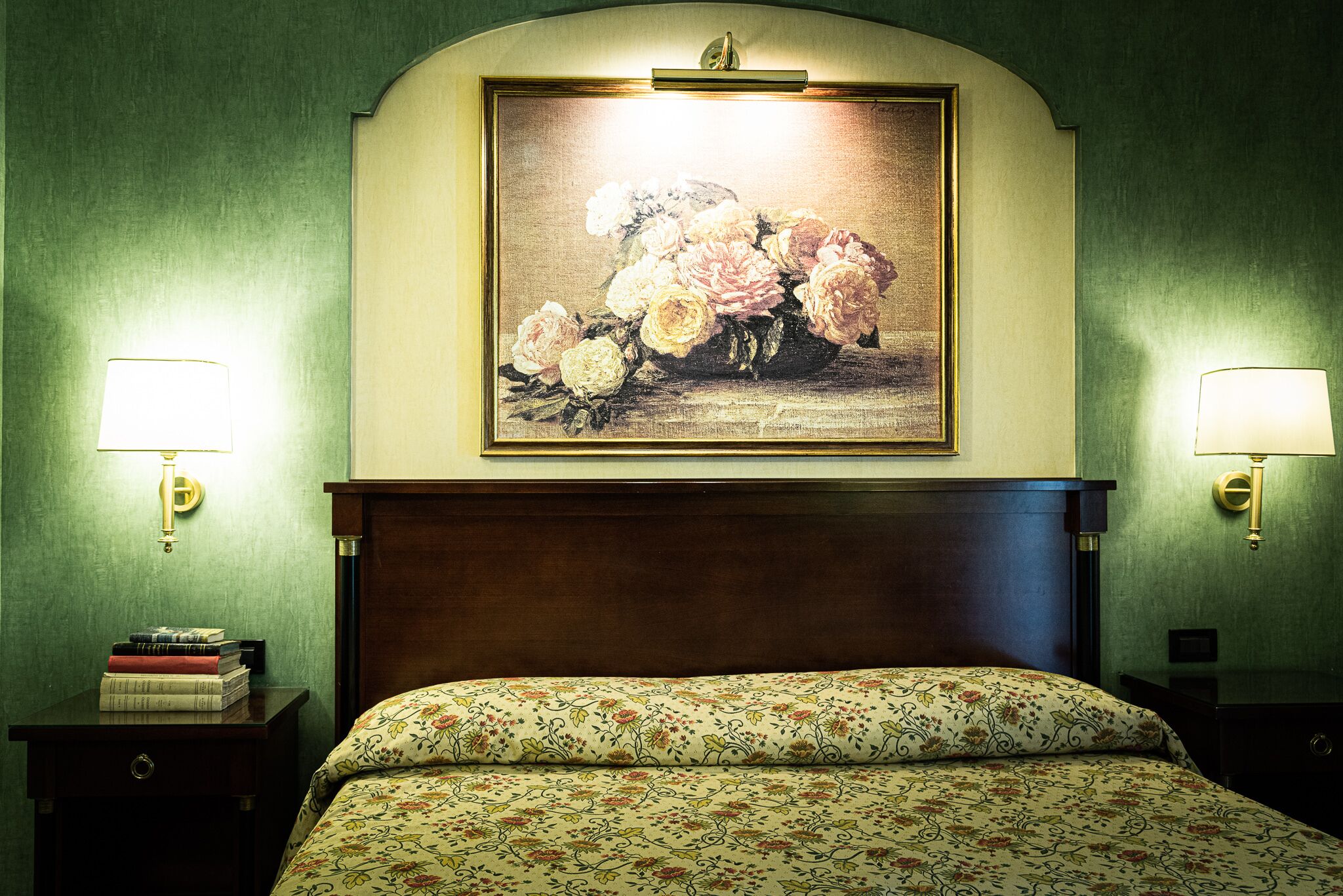 Una camera d'albergo con un letto, biancheria da letto a motivi floreali, un quadro floreale incorniciato sopra il letto e due lampade ai comodini.