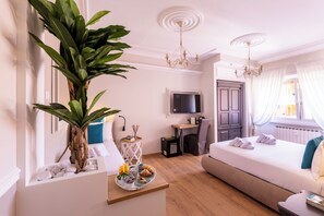 A hotel room with a bed, a desk, a television, a large plant, and a breakfast tray. - Trastevere Paper Suites (Rome)
