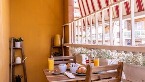 A wooden table set with breakfast items, a bench, and a view of a building through a window with a striped awning. - Trastevere Paper Suites (Rome)