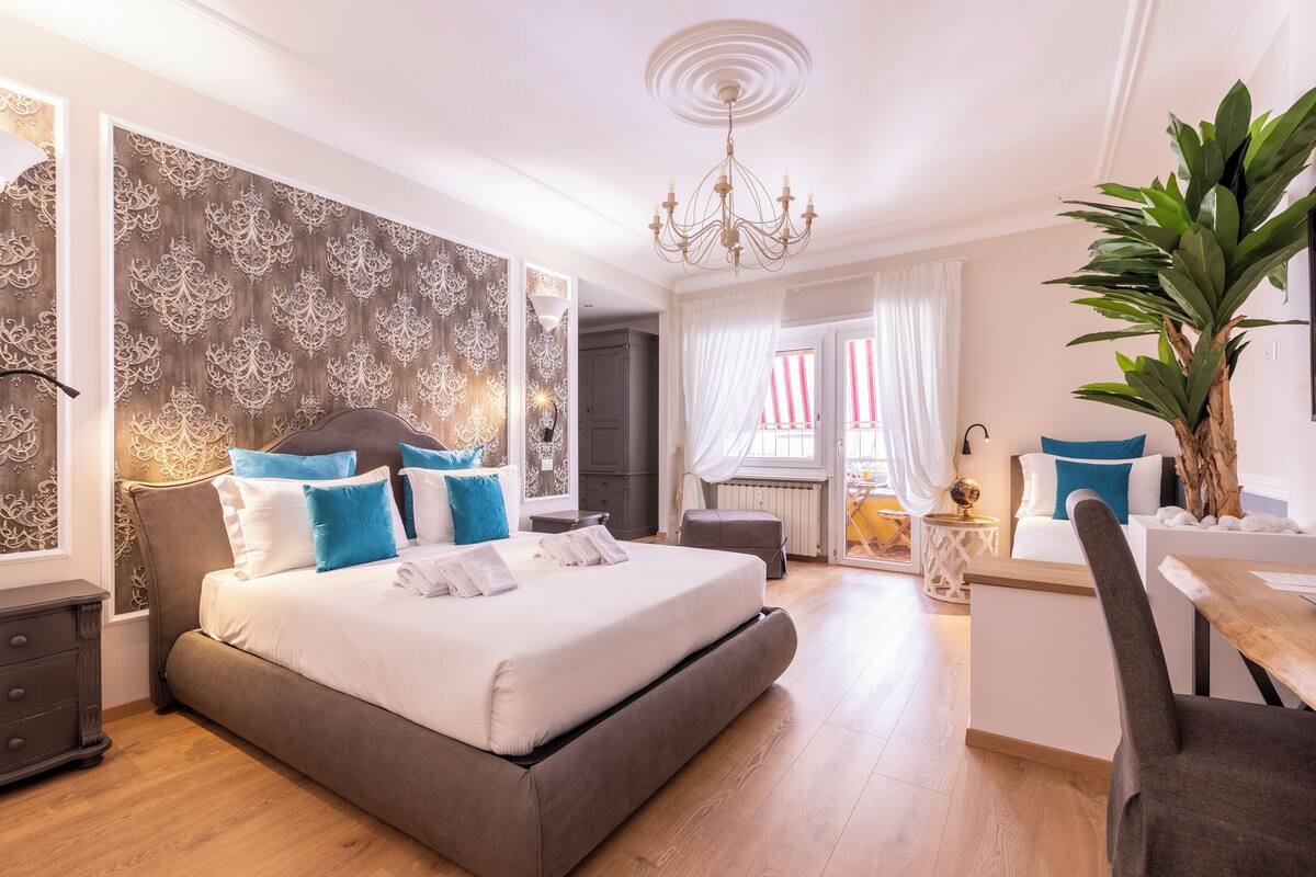 A modern bedroom with a large bed, bedside tables, a chandelier, and a potted plant.