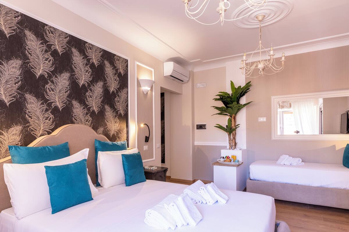 A hotel room with a large bed, a smaller bed, a potted plant, and a mirror.