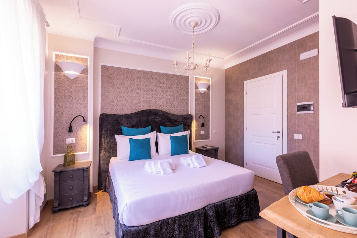A neatly arranged bedroom with a large bed, bedside tables, a chandelier, and a breakfast tray on a table.