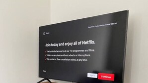Litteänäyttöinen televisio on sijoitettu harmaaseen TV-telineeseen, jonka päällä on puinen kansi.