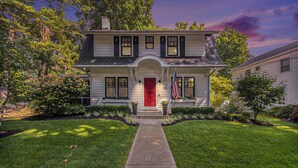 Une maison à deux étages avec une porte rouge, un porche à l’avant et une pelouse bien entretenue.