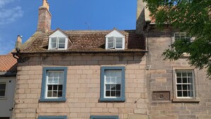 Un bâtiment en pierre de deux étages, doté de fenêtres à cadre bleu et d’une petite lucarne sur le toit.