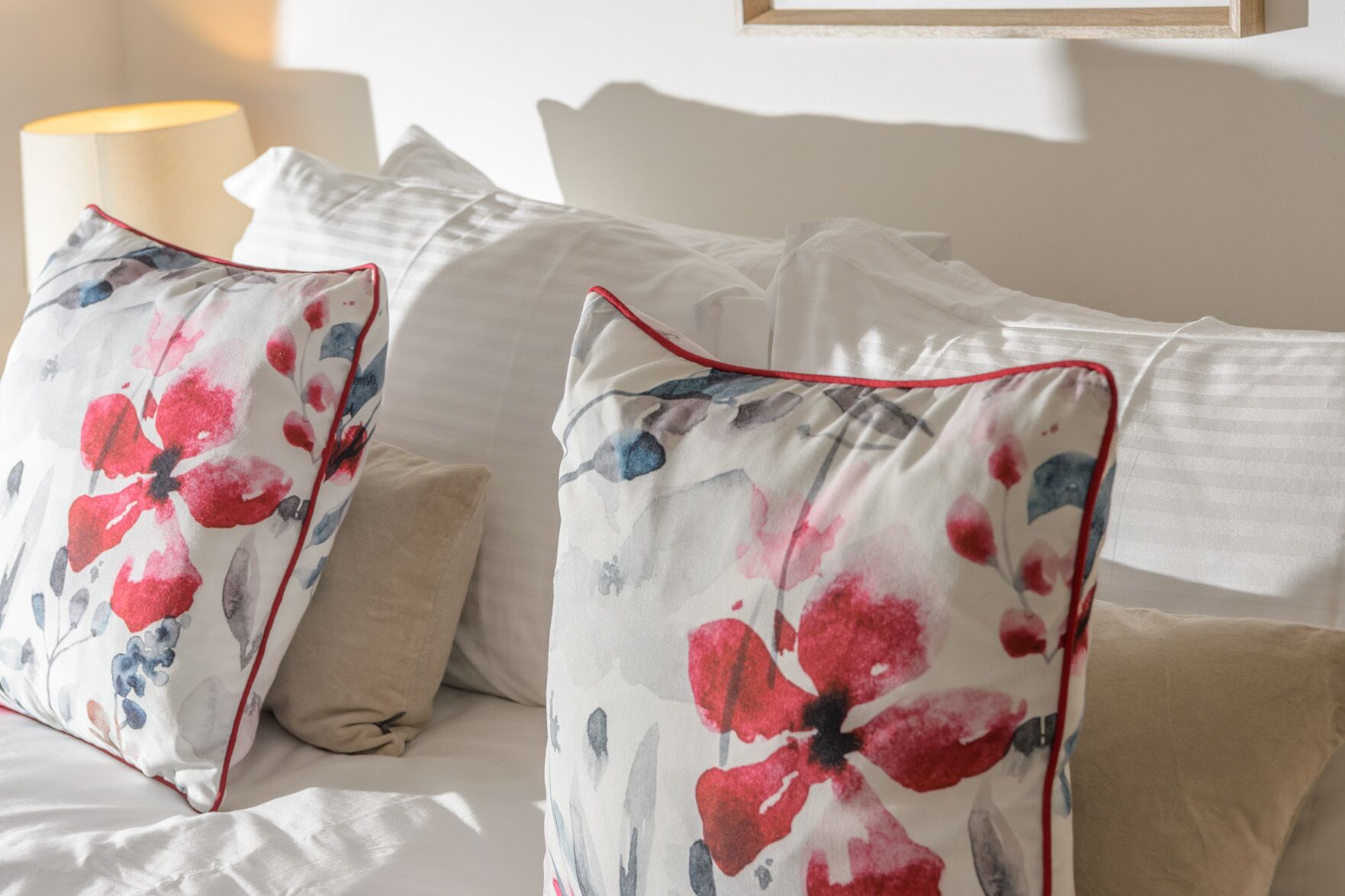 Een net opgemaakt bed met witte lakens en twee sierkussens met een bloemenmotief.