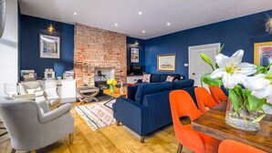 Un salon moderne avec une cheminée en briques, des murs bleus et un coin repas avec des chaises orange.