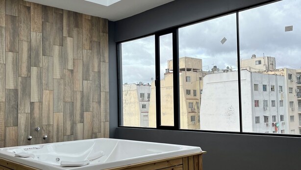A modern bathroom with a freestanding bathtub, wooden panel walls, and large windows offering a city view. - Luxury Studio in San Telmo (Buenos Aires)