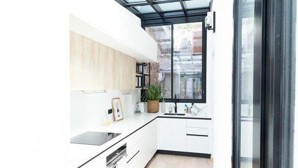 Eine moderne Küche mit weißen Schränken, einer schwarzen Arbeitsplatte, einem eingebauten Backofen und einem Fenster mit Blick ins Freie.