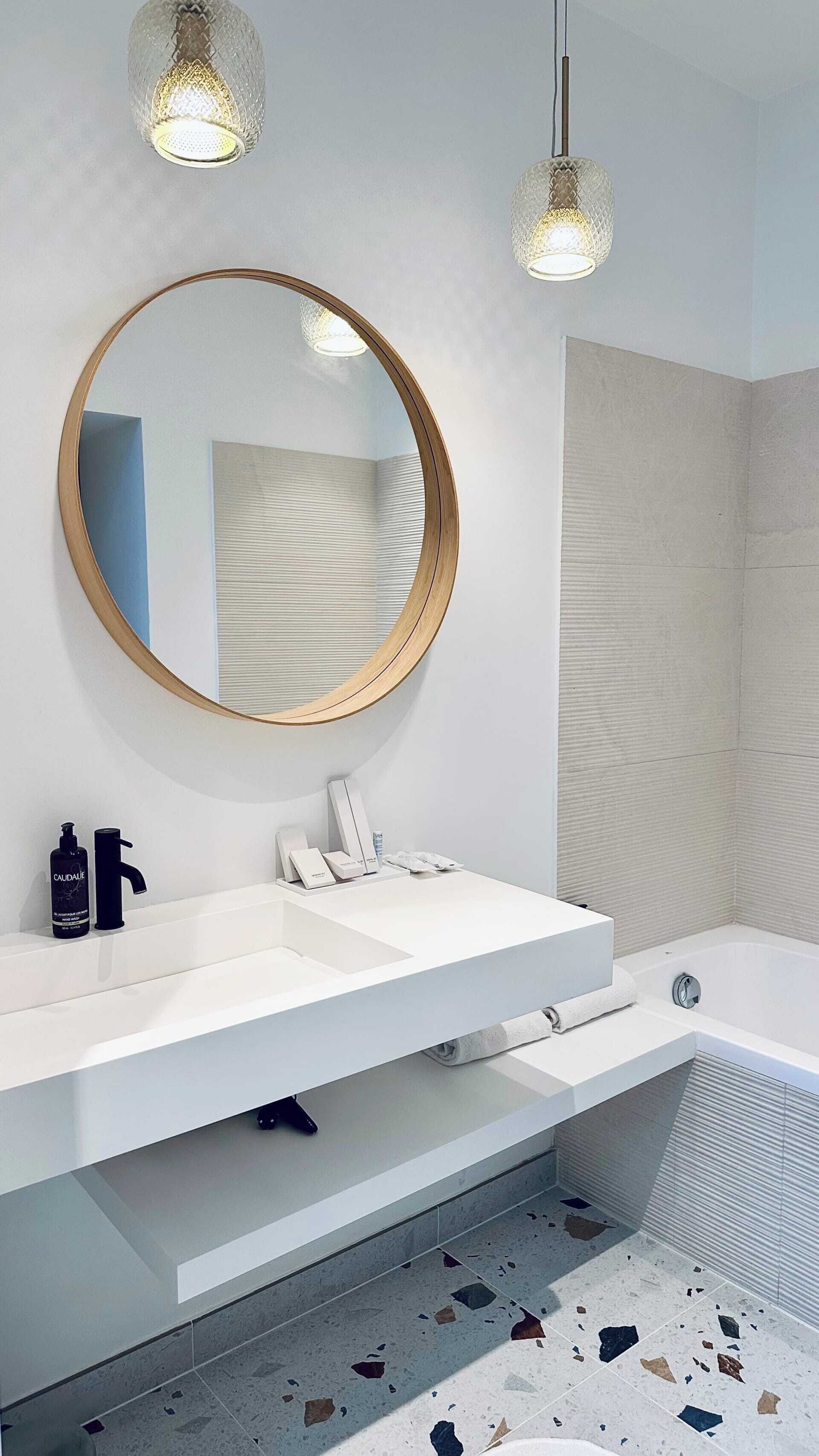 A modern bathroom with a round mirror, white vanity, and a bathtub.