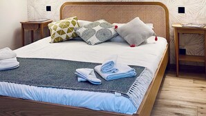 Ein Schlafzimmer mit einem hölzernen Bett, gemustertem Wandpapier, zwei Nachttischen und Pendelleuchten.