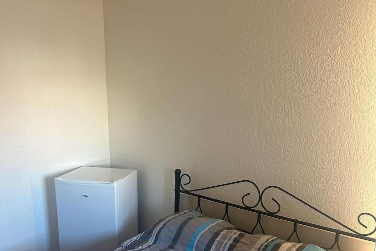 Una cama individual con una colcha a rayas, una mesita de noche blanca y un aplique de pared.