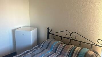 A single bed with a striped blanket, a white bedside table, and a wall-mounted light fixture.
