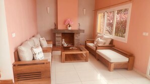 A living room with a fireplace, two sofas, a coffee table, and a window with a view. - Room in Villa - Comfortable and Welcoming Suite With Terrace Overlooking the Lake (Antananarivo)