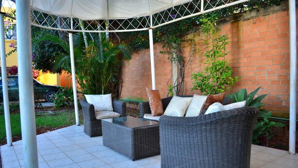 A covered patio area with wicker furniture and a brick wall. - Room in Villa - Comfortable and Welcoming Suite With Terrace Overlooking the Lake (Antananarivo)