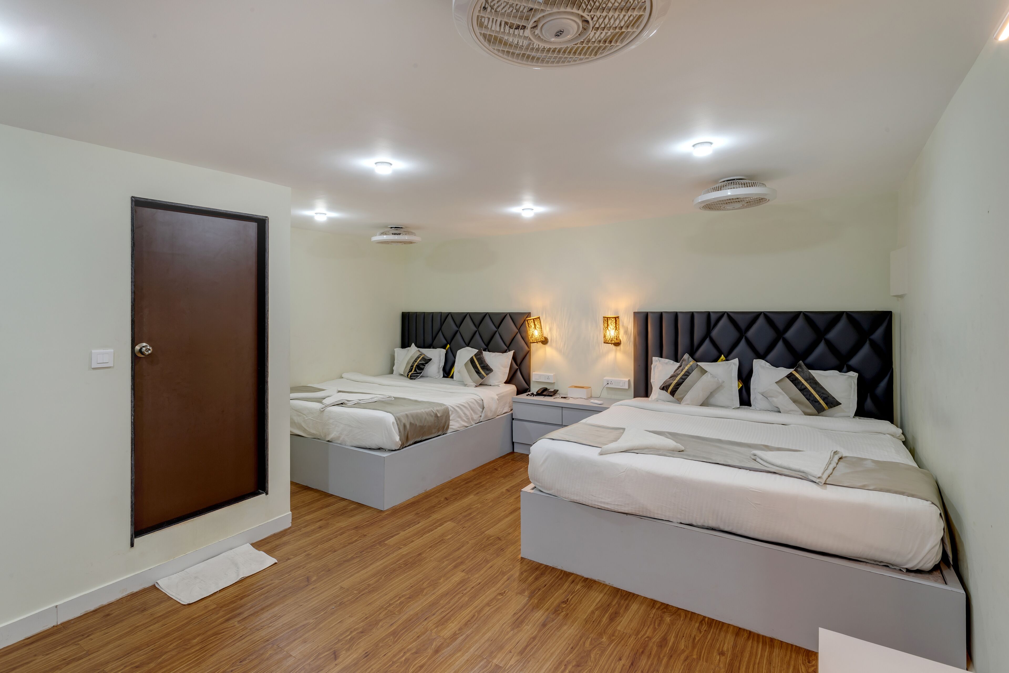 A hotel room with two beds, a wooden floor, a ceiling fan, and recessed lighting.