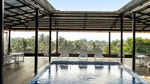Une piscine intérieure avec vue sur les palmiers, entourée de chaises et de tables blanches sous une toiture métallique.