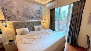A hotel room with a large bed, a wall-mounted air conditioner, and a view of the outdoors through a sliding glass door. -  La Baga Beach Hotel (Calangute)