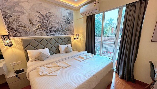 Een hotelkamer met een groot bed, een wandairconditioner en uitzicht op het groen door een schuifdeur.