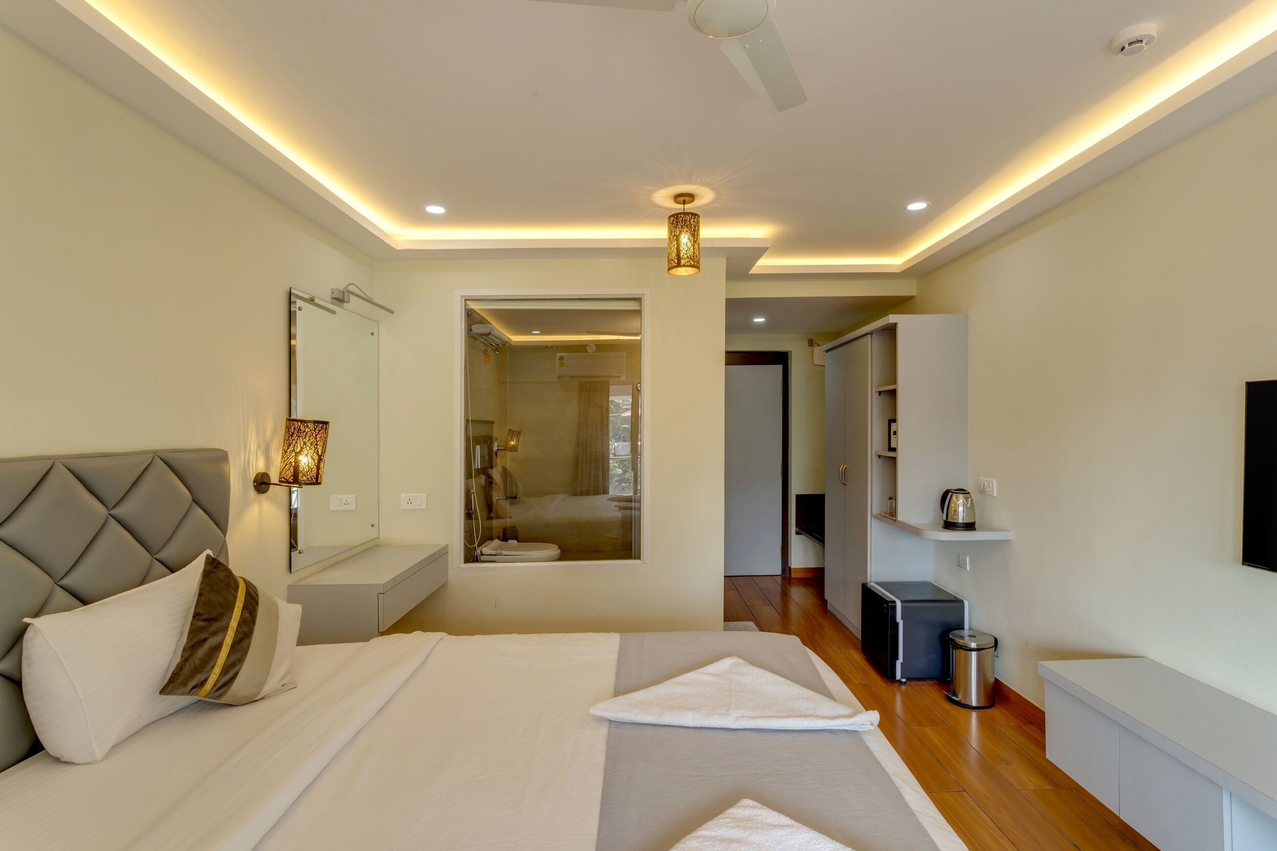 Una habitación de hotel moderna con una cama grande, una mesita de noche, un espejo, un ventilador de techo y un televisor montado en la pared.