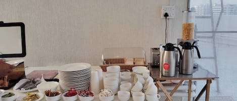 A breakfast setup with plates, cups, and a coffee maker on a table near a window.