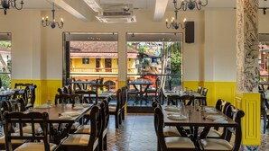 A restaurant with multiple tables and chairs, a view of buildings outside, and a patterned wall on the right. -  La Baga Beach Hotel (Calangute)