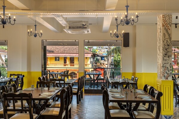 Un restaurant avec plusieurs tables et chaises, une vue sur les bâtiments à l’extérieur et un mur orné de motifs sur le côté droit.