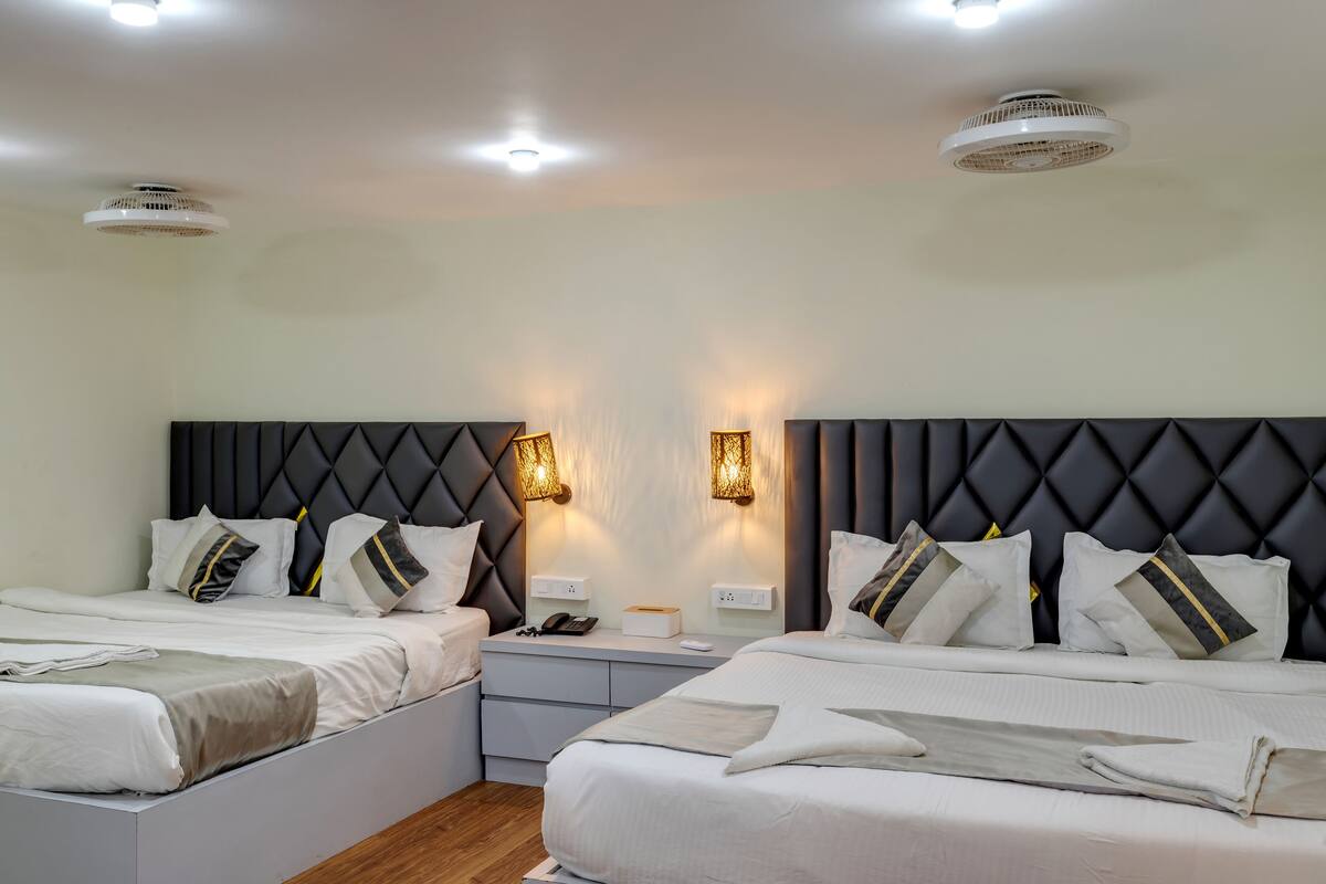 Een moderne slaapkamer met twee bedden, een donker hoofdeinde, bedlampen en een nachtkastje met een telefoon en doos.