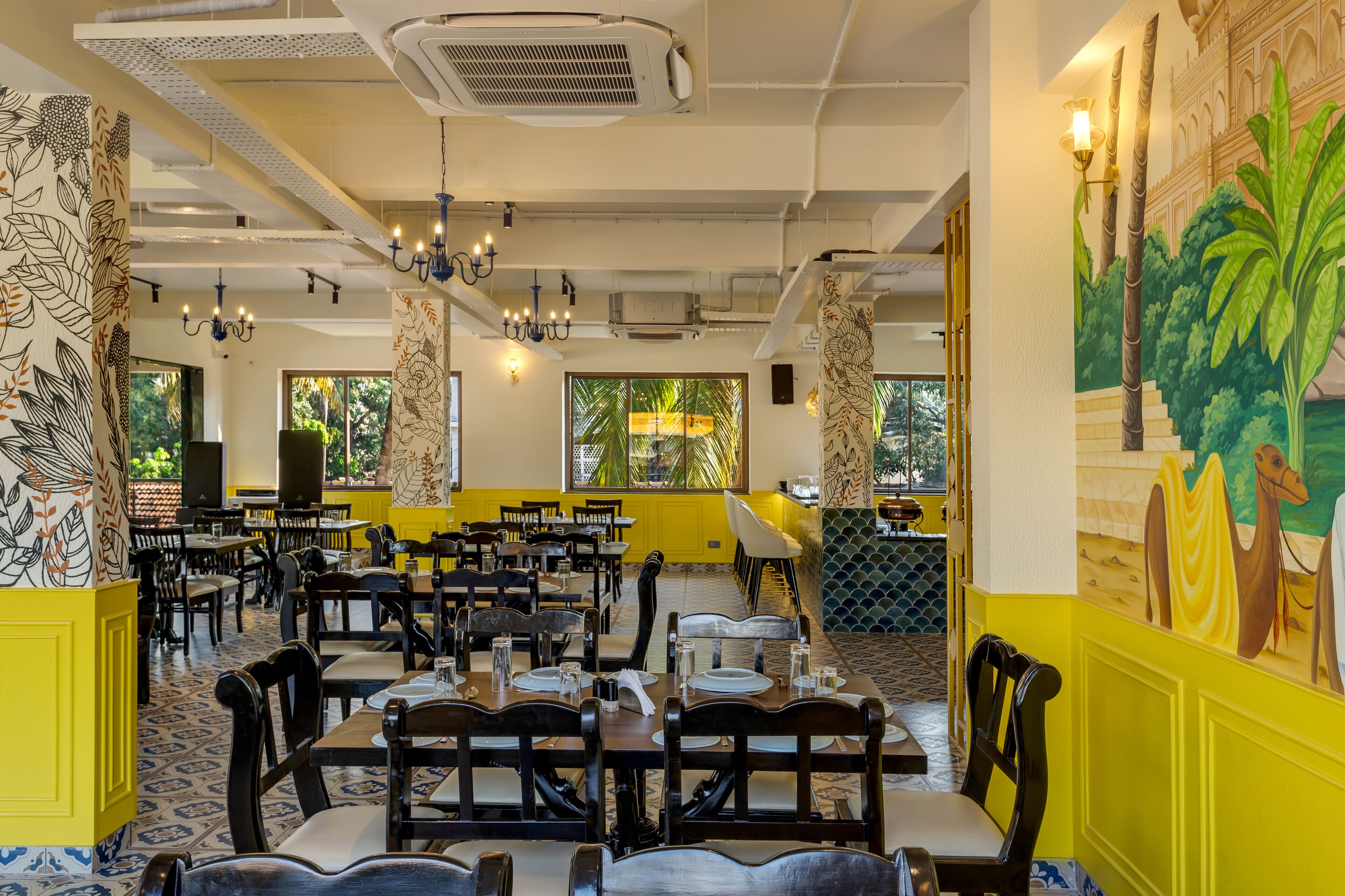 Un restaurante con varias mesas y sillas, paredes amarillas y murales decorativos.